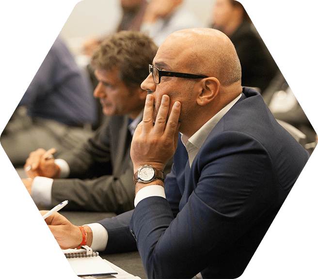 A man seated in the audience of a conference speaking event listening and taking notes