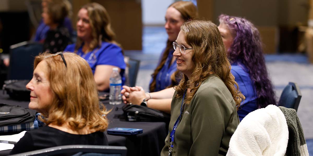 Women smiling and watching a presenter from their table. 