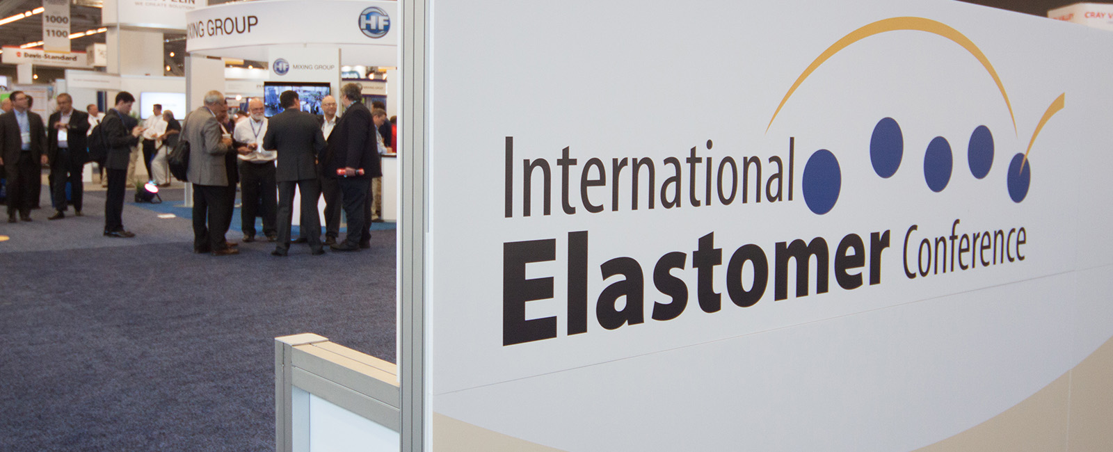 Conference attendees gathering at booths behind International Elastomer Conference indoor floor signage