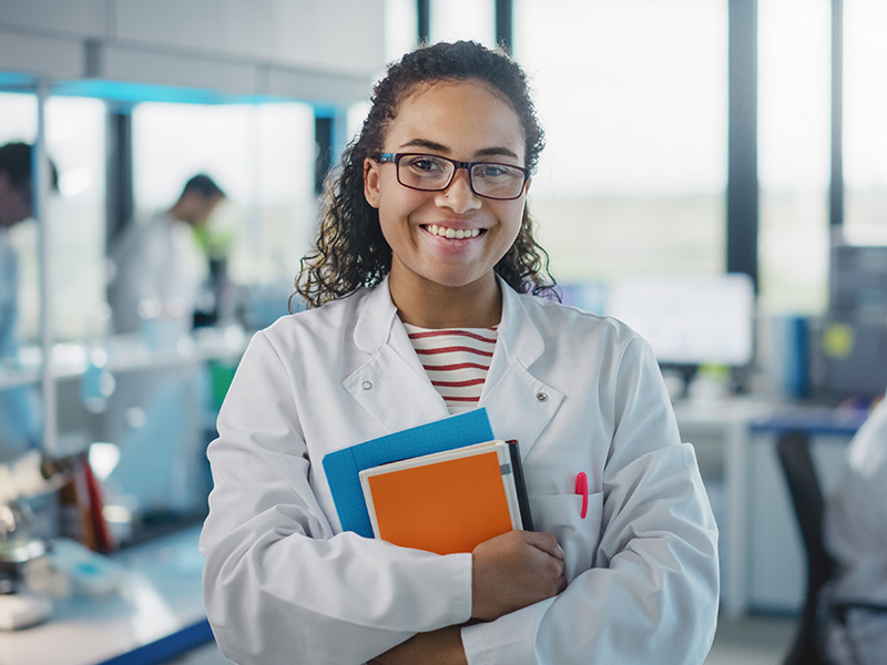 Female student in a lab wearing lab coat and holding notebooks